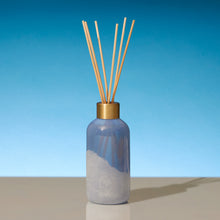 Reed diffuser with wooden sticks in a blue bottle against a blue background