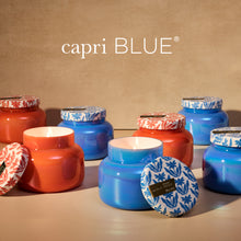 Colorful candles with decorative lids on a beige background, featuring the 'capri BLUE' brand.