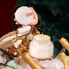 Pumpkin Dulce Holiday Mercury Signature Scented Candle held by woman surrounded by champagne bottles