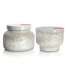 Two glass scented candle jars with decorative lids on a white background