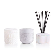 Set of two candles and a white diffuser with black reeds on a white background