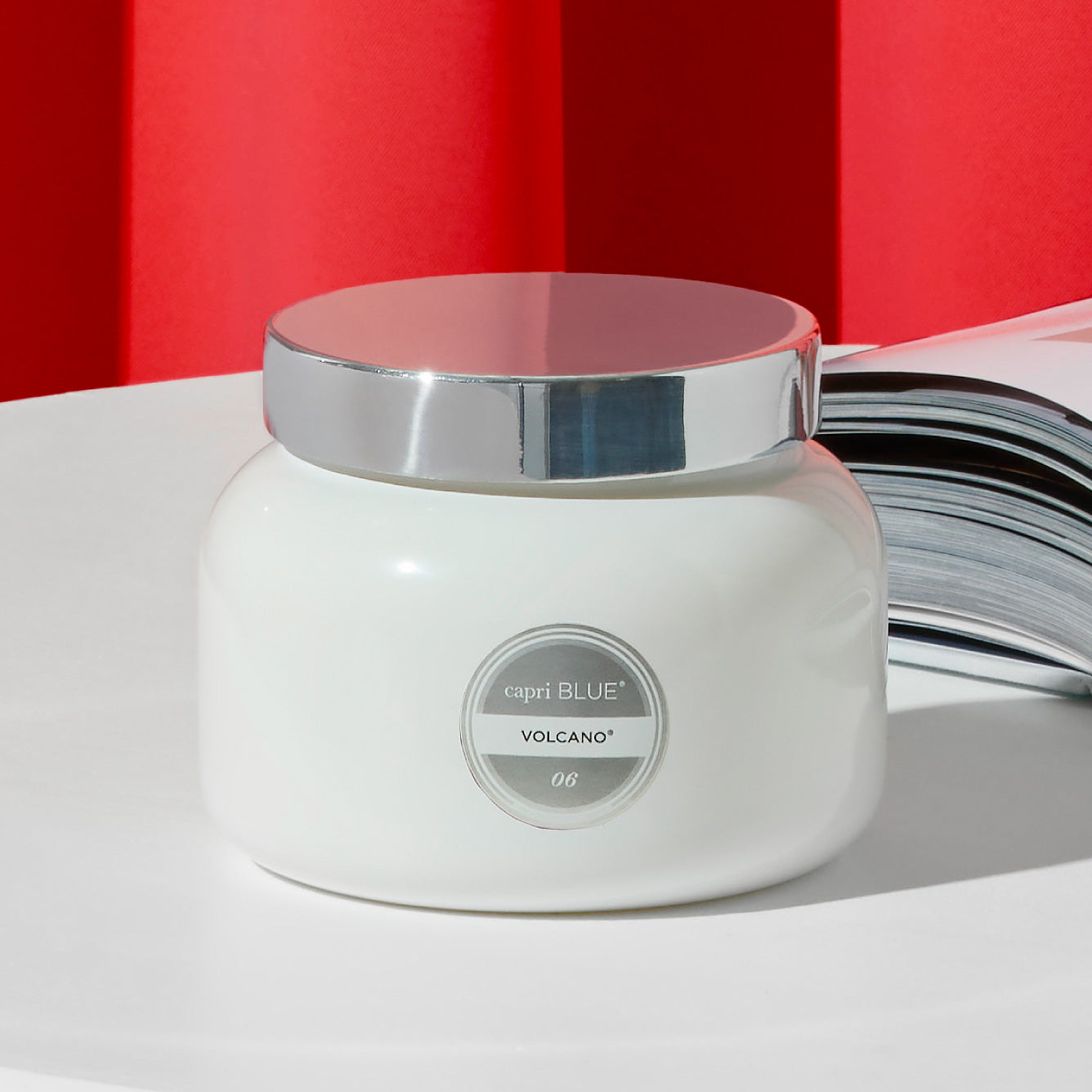 White candle jar with silver lid on a white surface against a red background