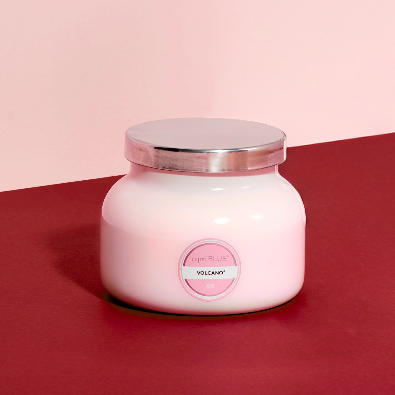 Pink candle jar with a silver lid on a red and pink gradient background