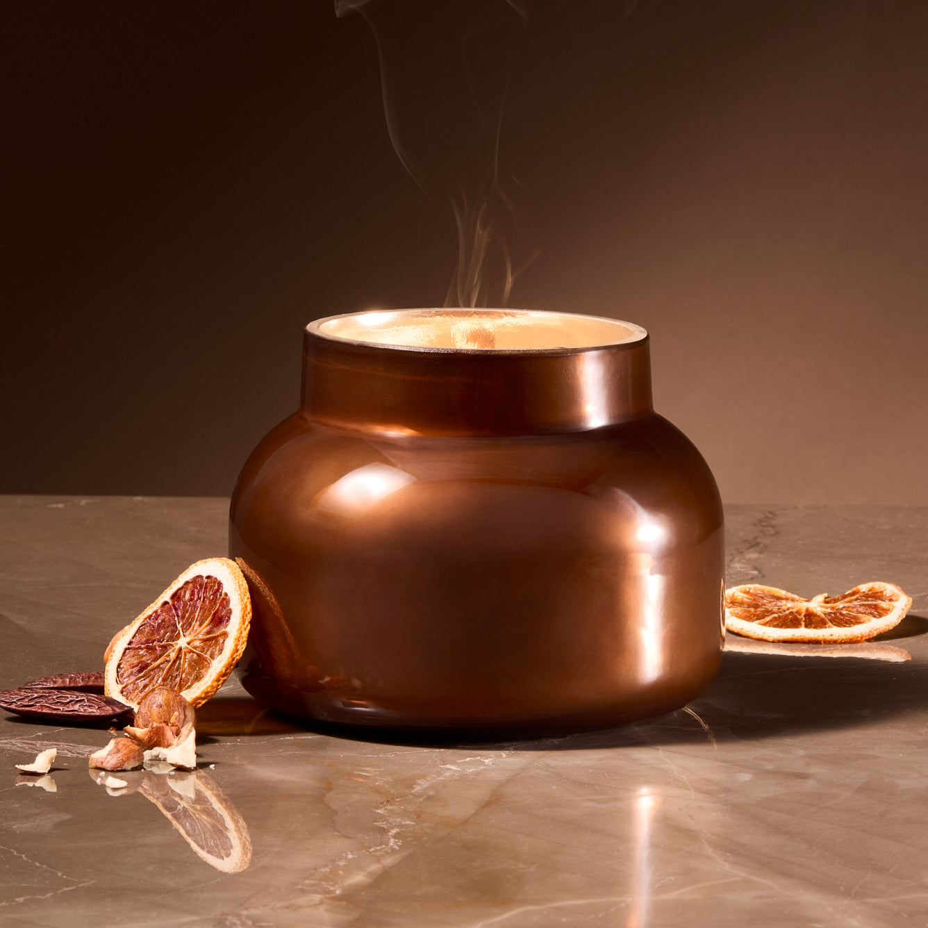 Autumn Glow Chestnut Embers Signature Candle with dried citrus fruit on a marble surface