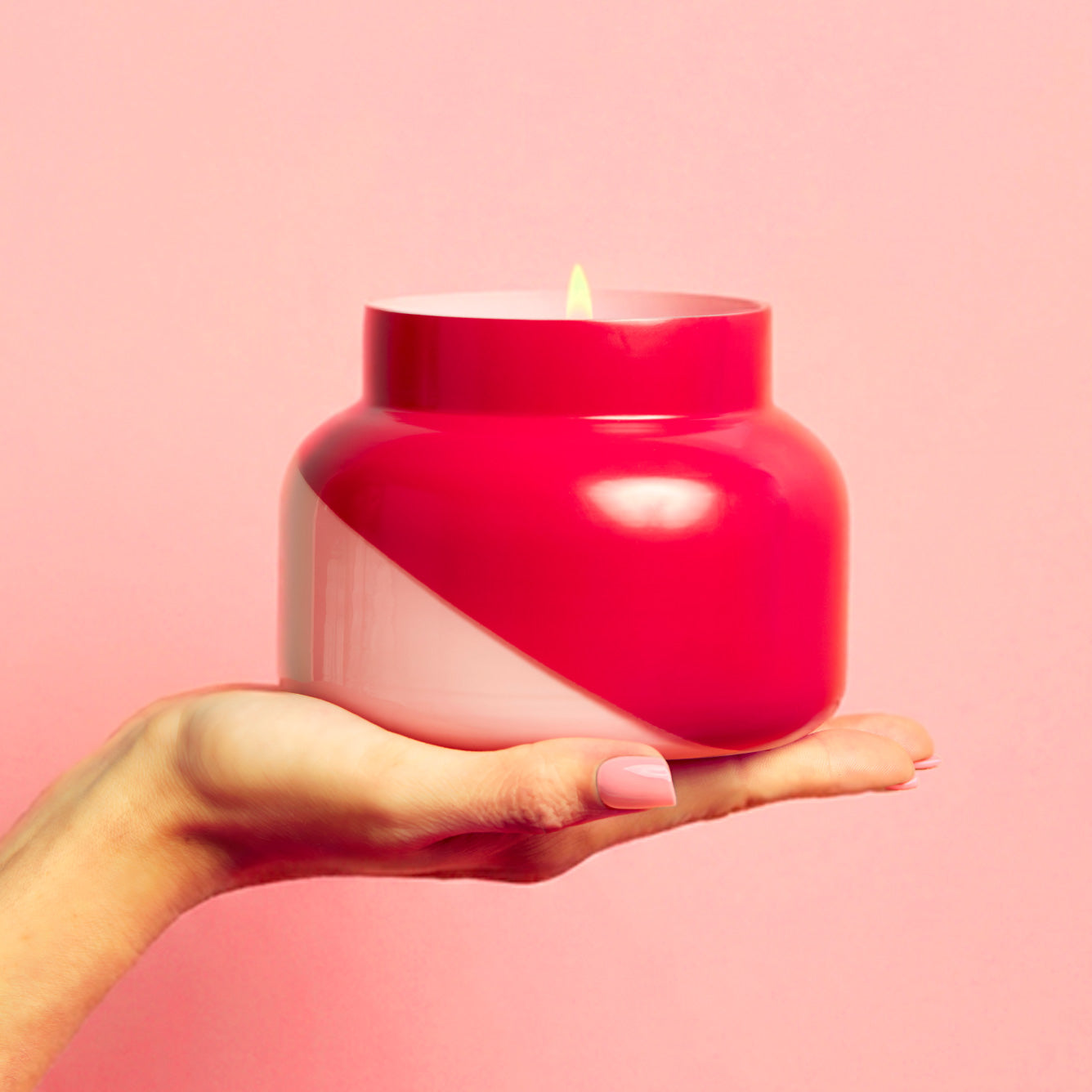 Hand holding a pink candle jar against a pink background