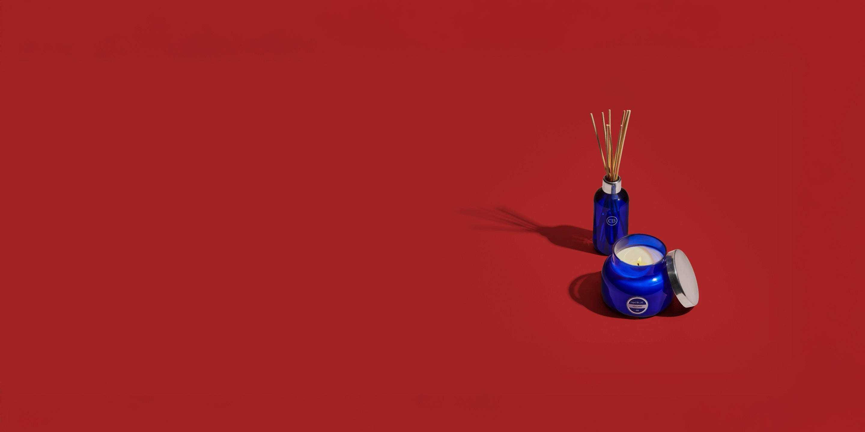 Blue candle jar with a reed diffuser on a red background