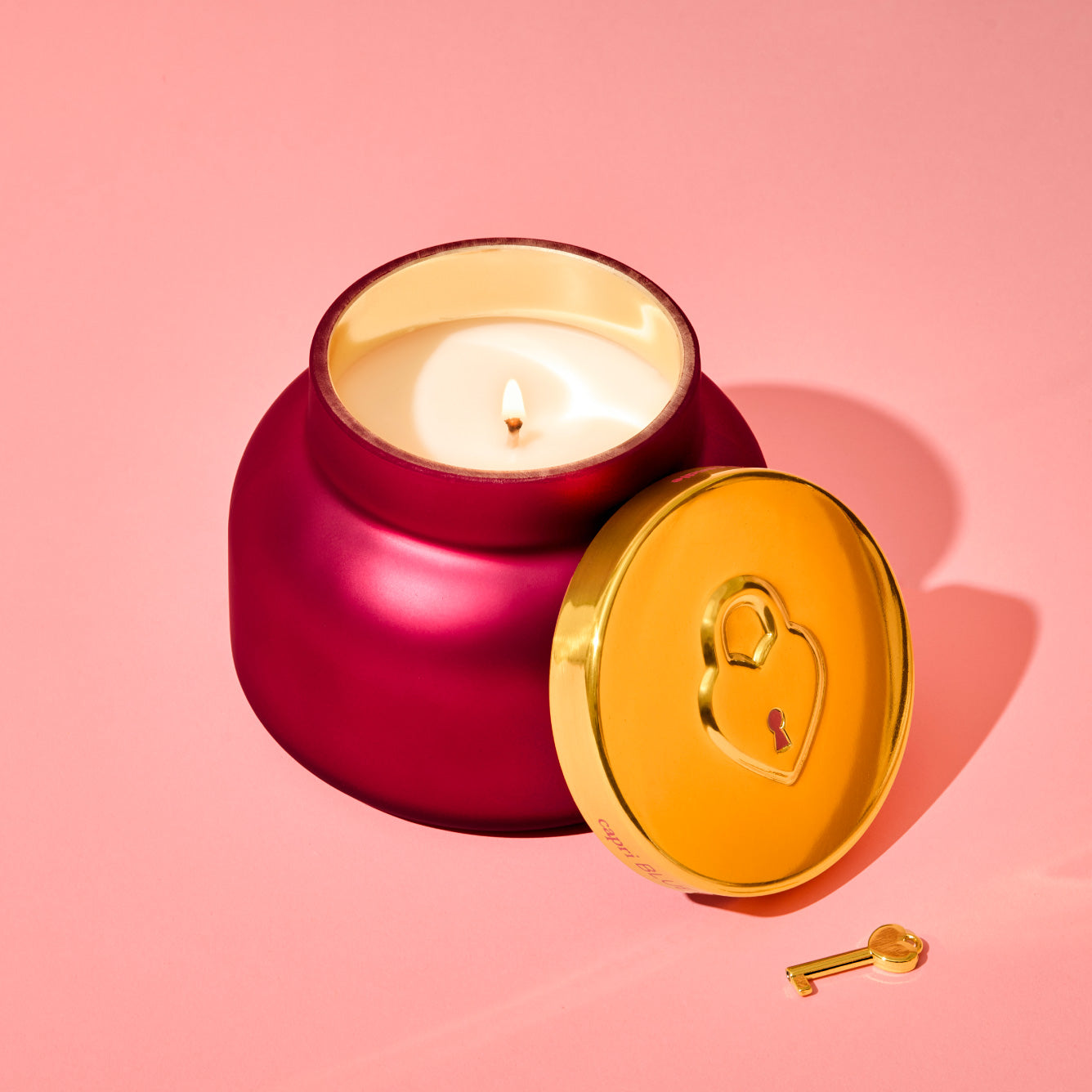 Red candle in a gold holder with a heart-shaped key on a pink background