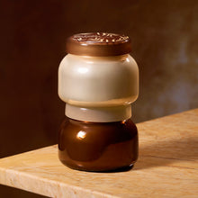 Two glass scented candle jars with lids stacked on a marble table