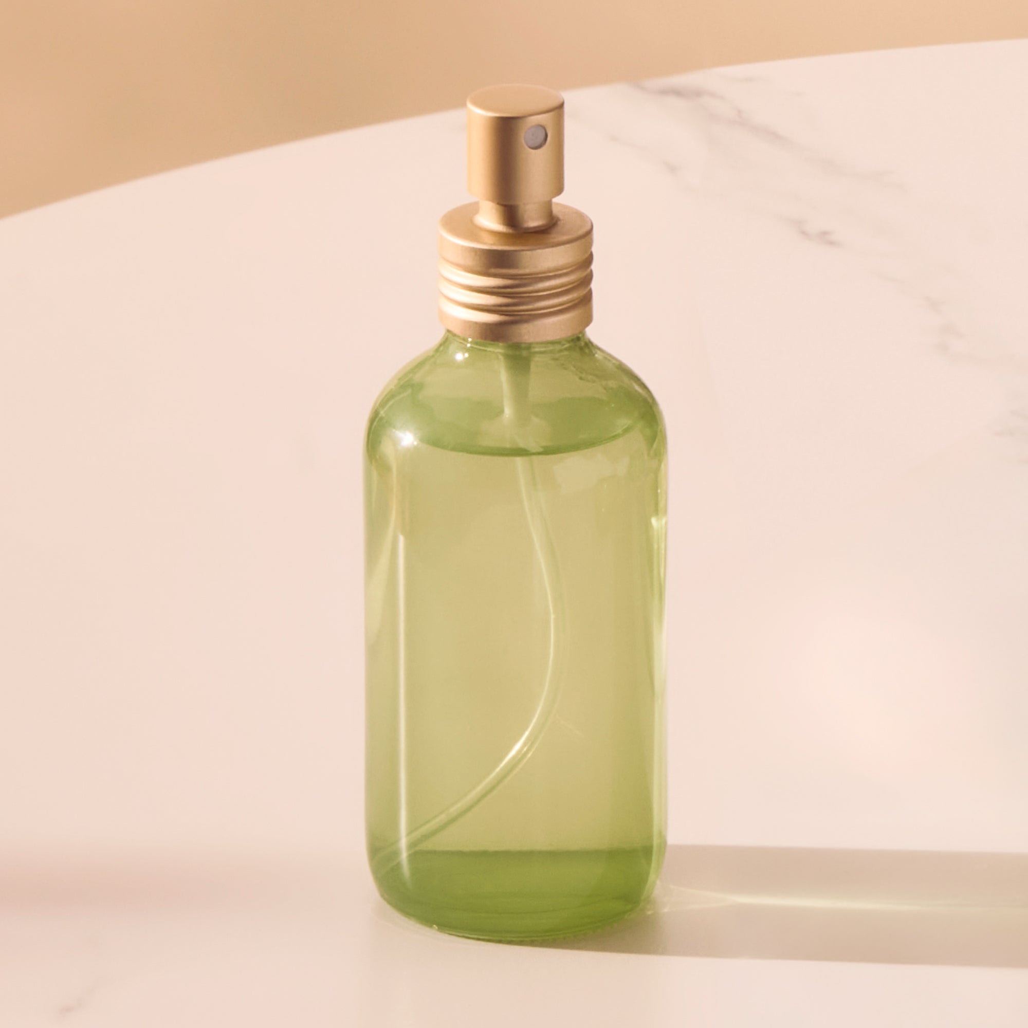Green spray bottle with gold nozzle on a beige background