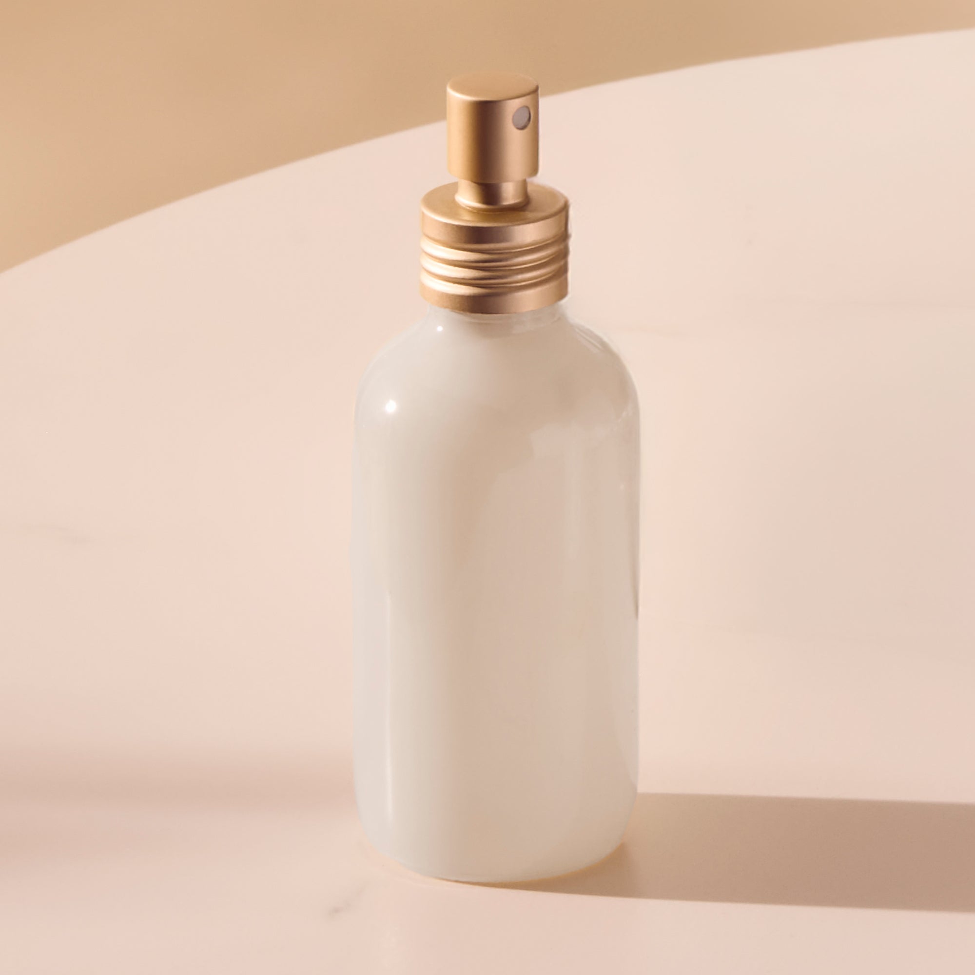 White ceramic bottle with gold cap on a beige background