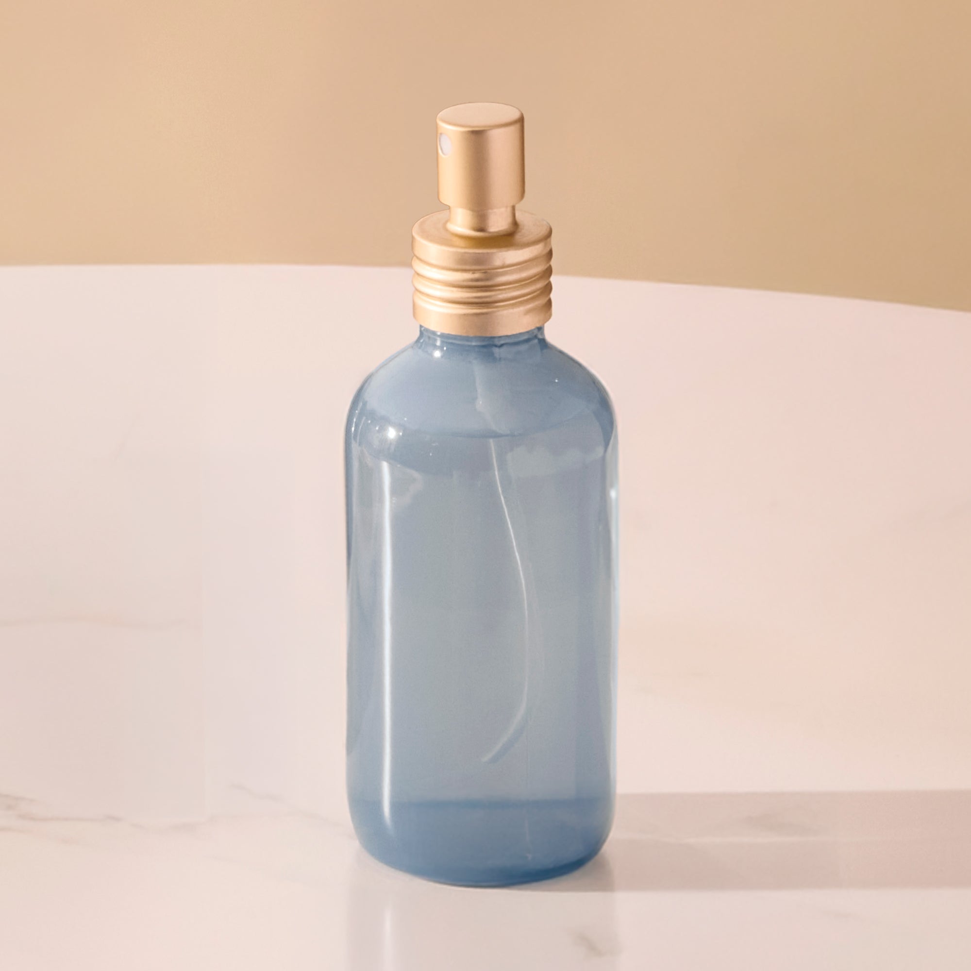 Blue spray bottle with gold nozzle on a light surface