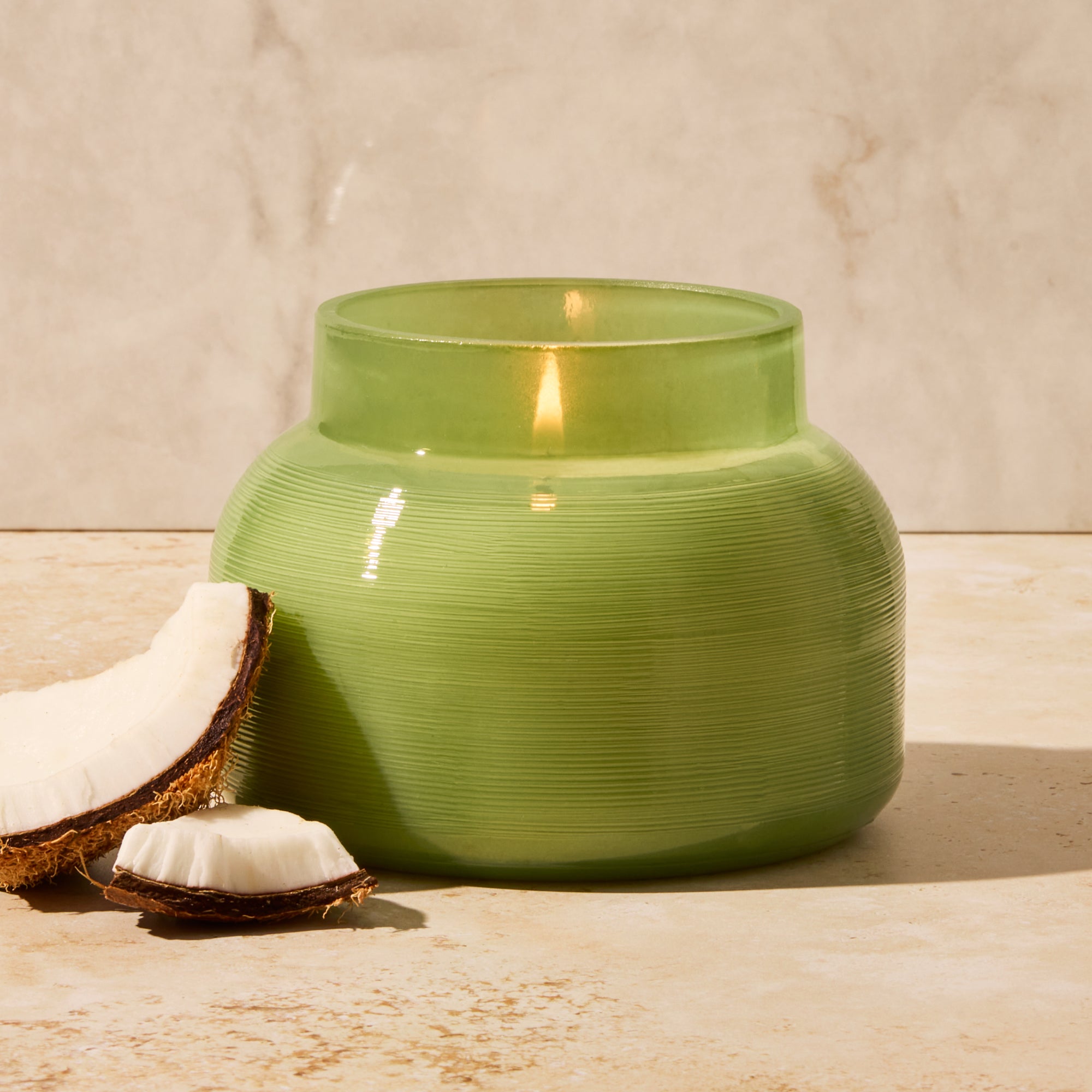 Green ceramic jar with a candle inside on a wooden surface with a light background