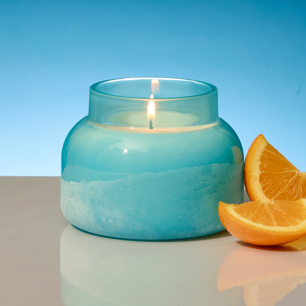 Blue candle in a glass jar with orange slices on a reflective surface and blue background