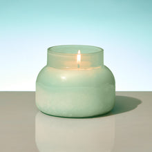 Light green candle in a glass jar on a reflective surface with a light blue gradient background