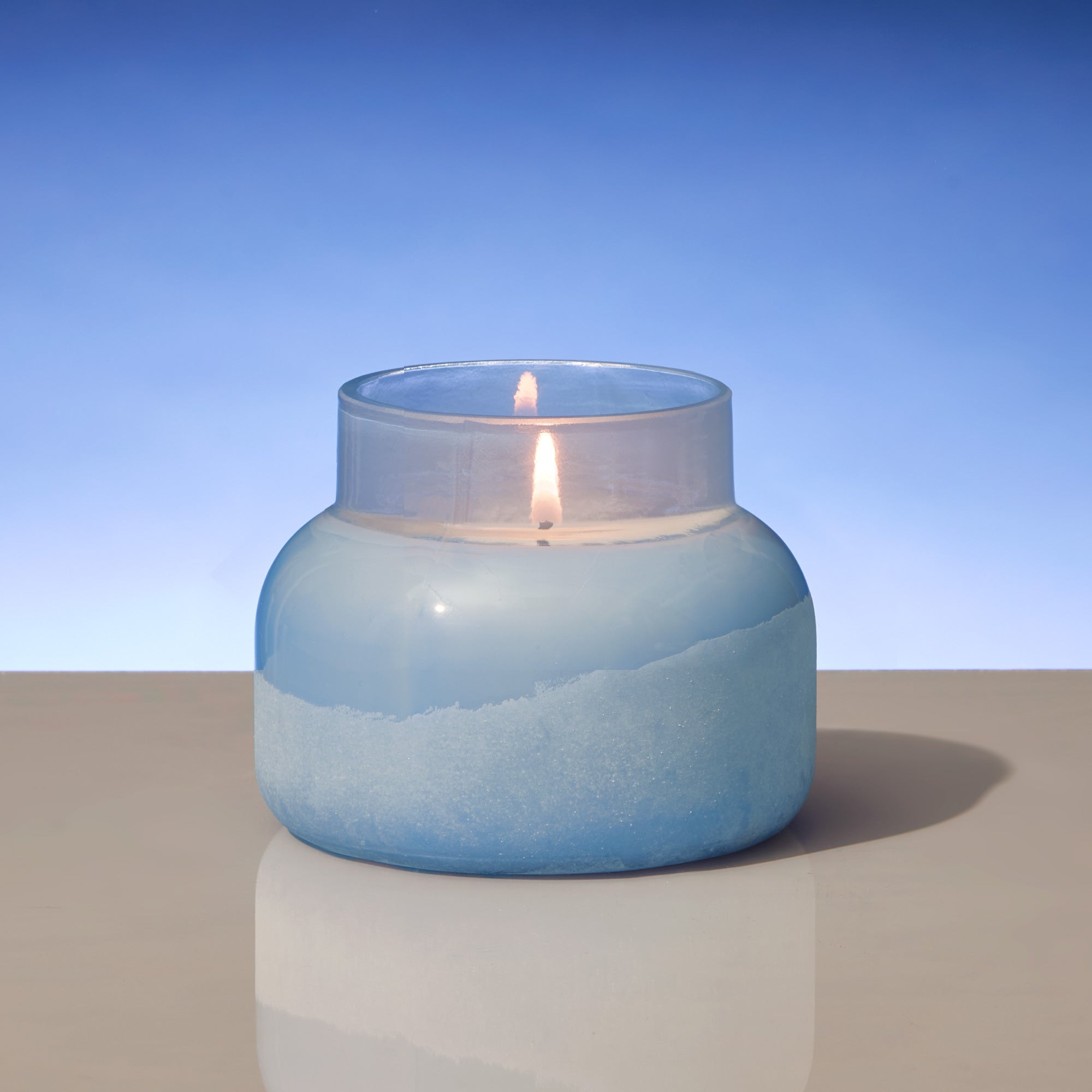 Candle in a blue glass jar with a gradient effect on a plain background