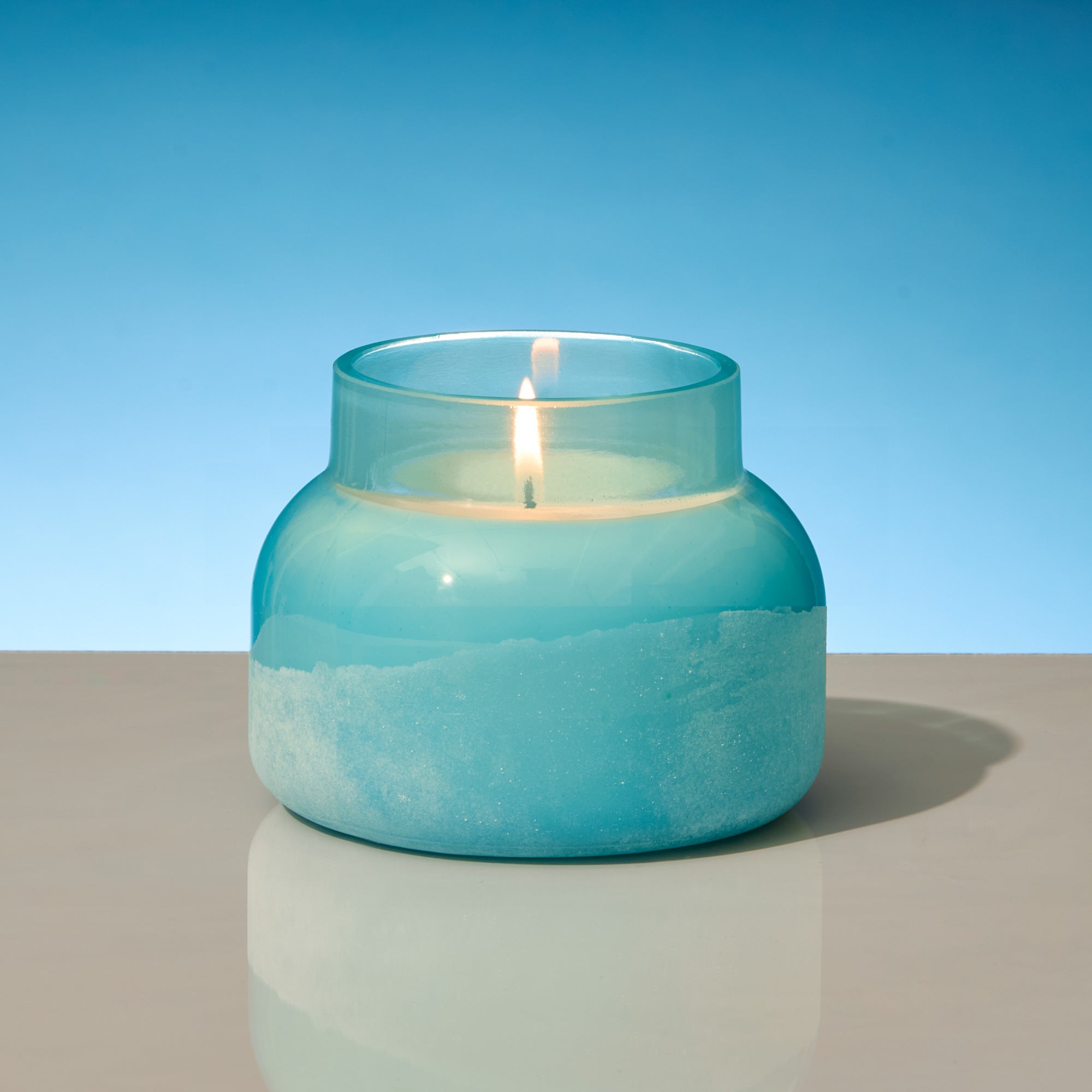 Candle in a blue glass jar on a reflective surface with a blue background