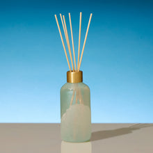 Reed diffuser with gold cap on a blue gradient background
