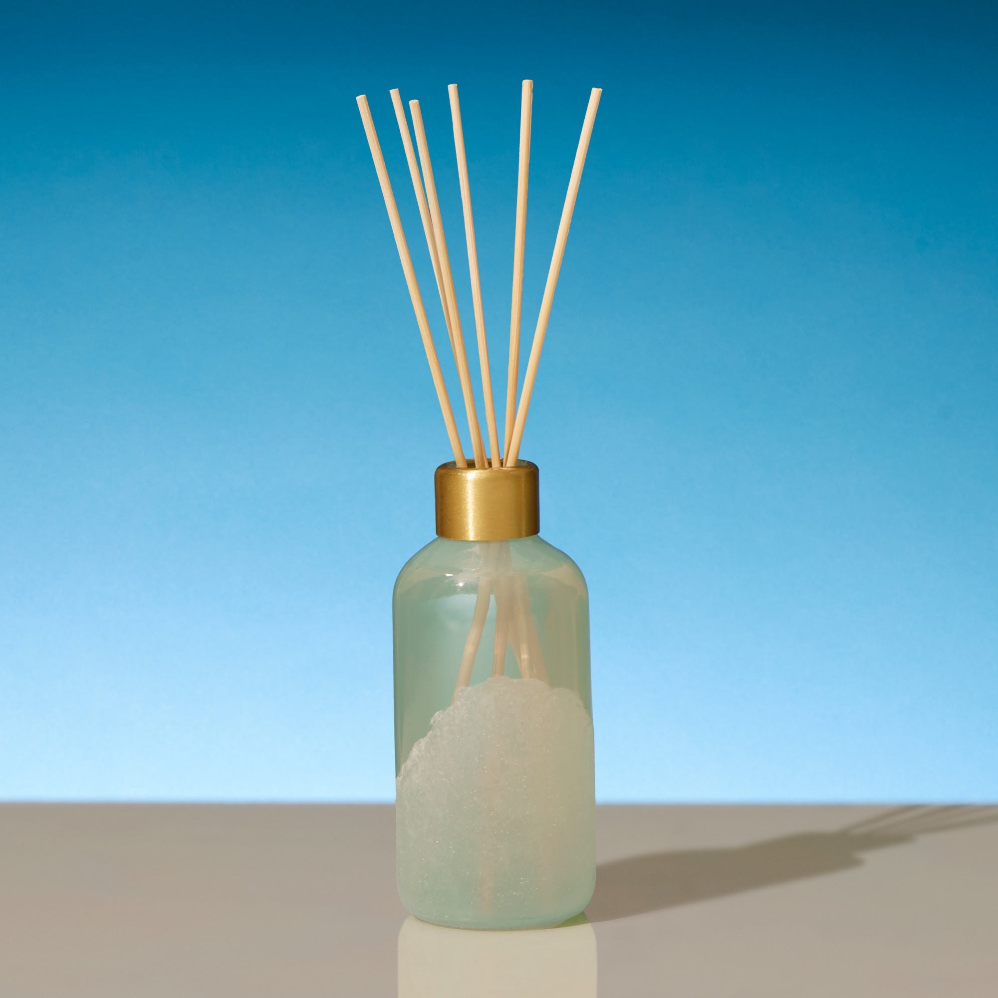 Reed diffuser with gold cap on a blue gradient background