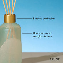 Decorative diffuser bottle with gold collar and sea glass texture on a blue background