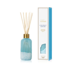 Reed diffuser with blue bottle and gold cap next to its packaging on a white background