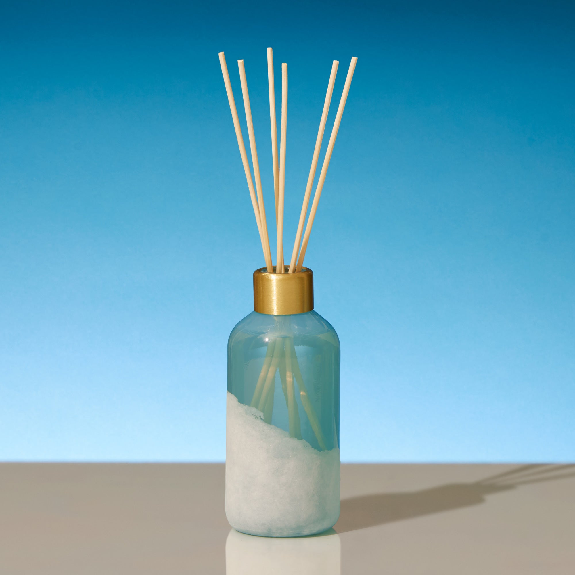 Reed diffuser with wooden sticks in a blue bottle against a clear blue sky