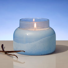 Blue glass candle with a vanilla bean on a light surface and blue background