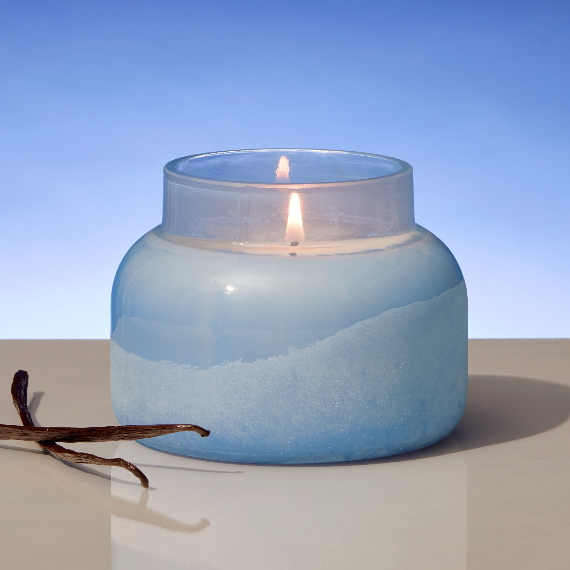 Blue glass candle with a vanilla bean on a light surface and blue background