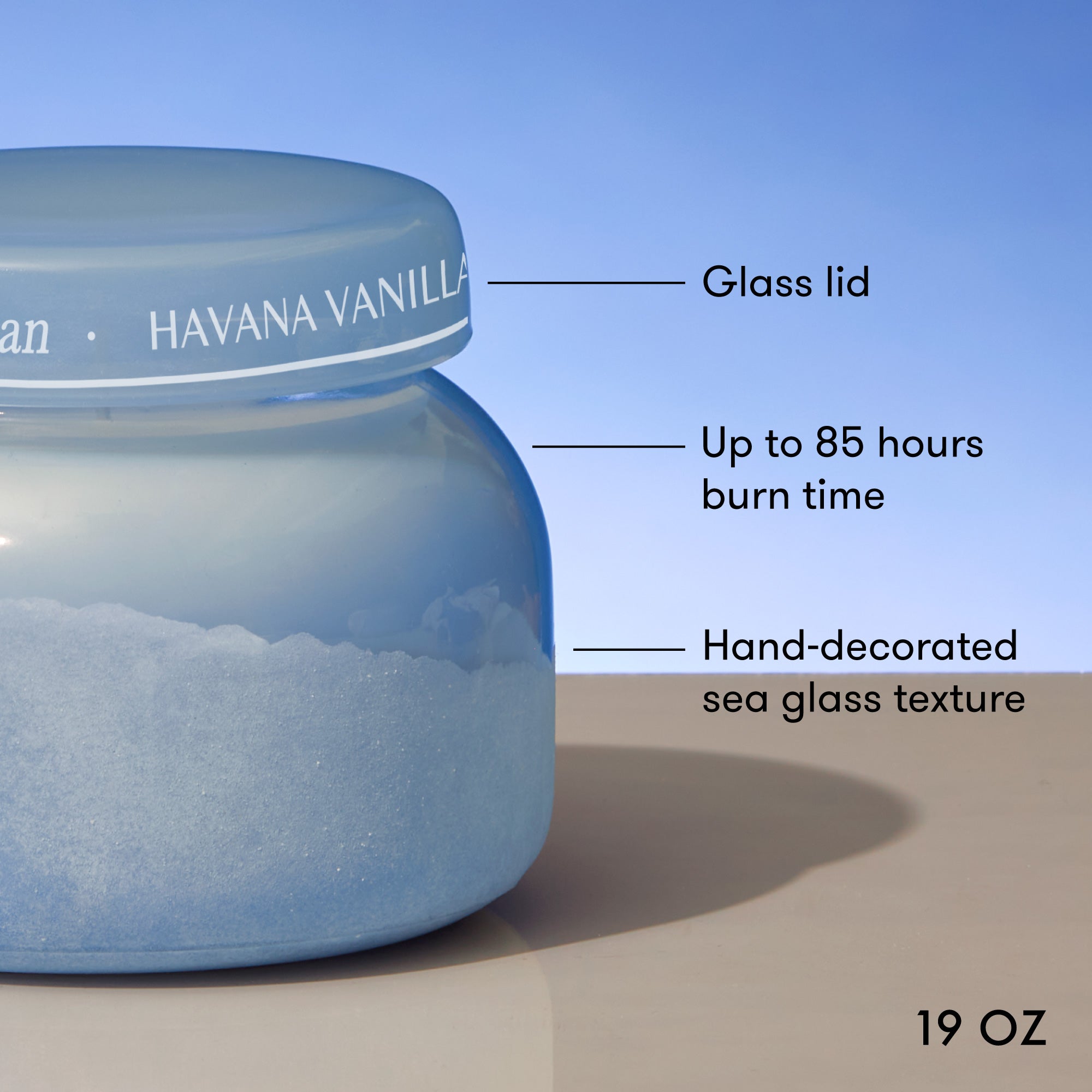 Blue candle jar with decorative lid labeled 'Havana Vanilla' on a beige surface with blue background.