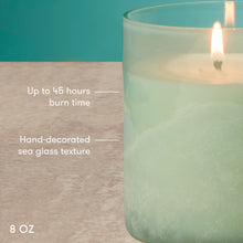 Lighted candle in a textured glass container with text indicating burn time and size.