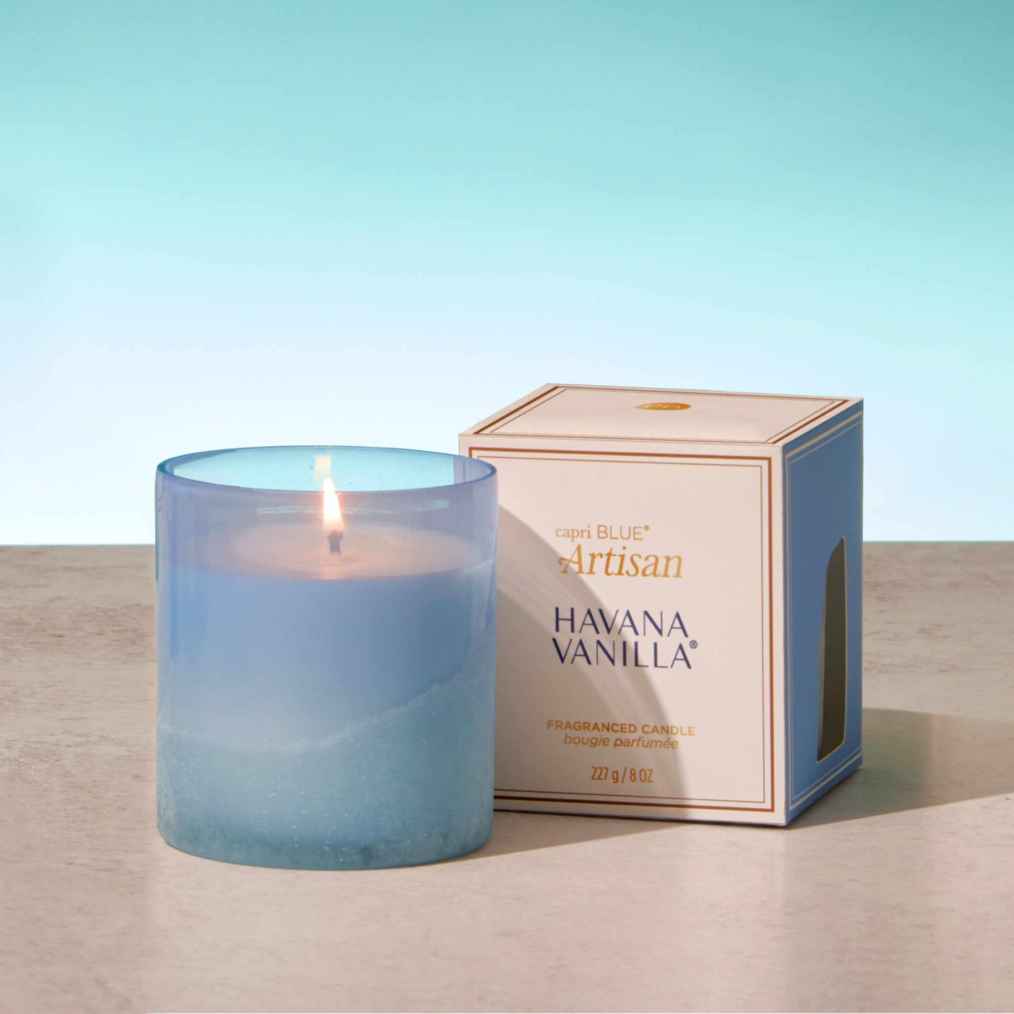 Blue candle with a lit wick next to its packaging on a wooden surface.