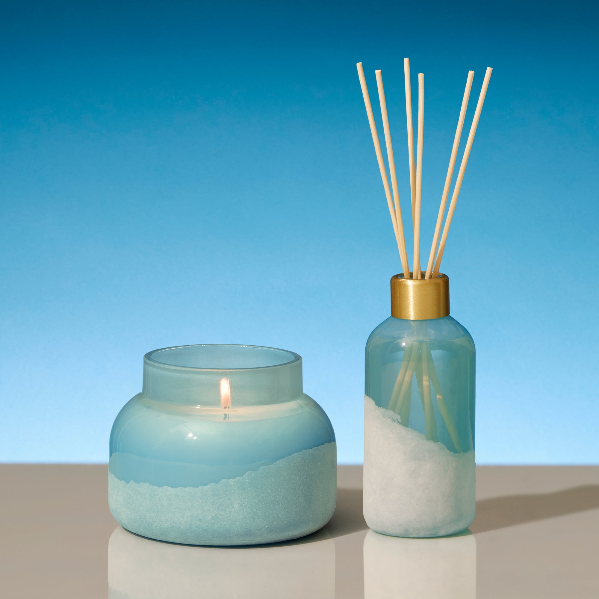 Candle and diffuser set with blue and white design on a reflective surface and blue background