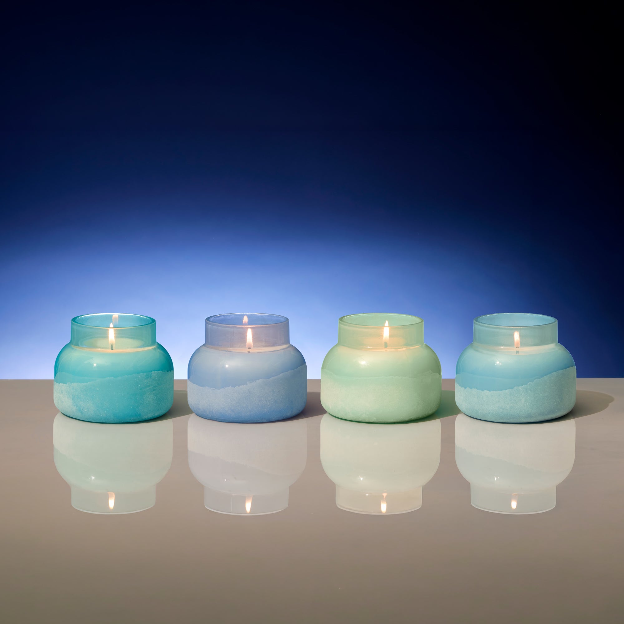 Four lit candles in glass jars with blue and green gradient on a reflective surface and blue background