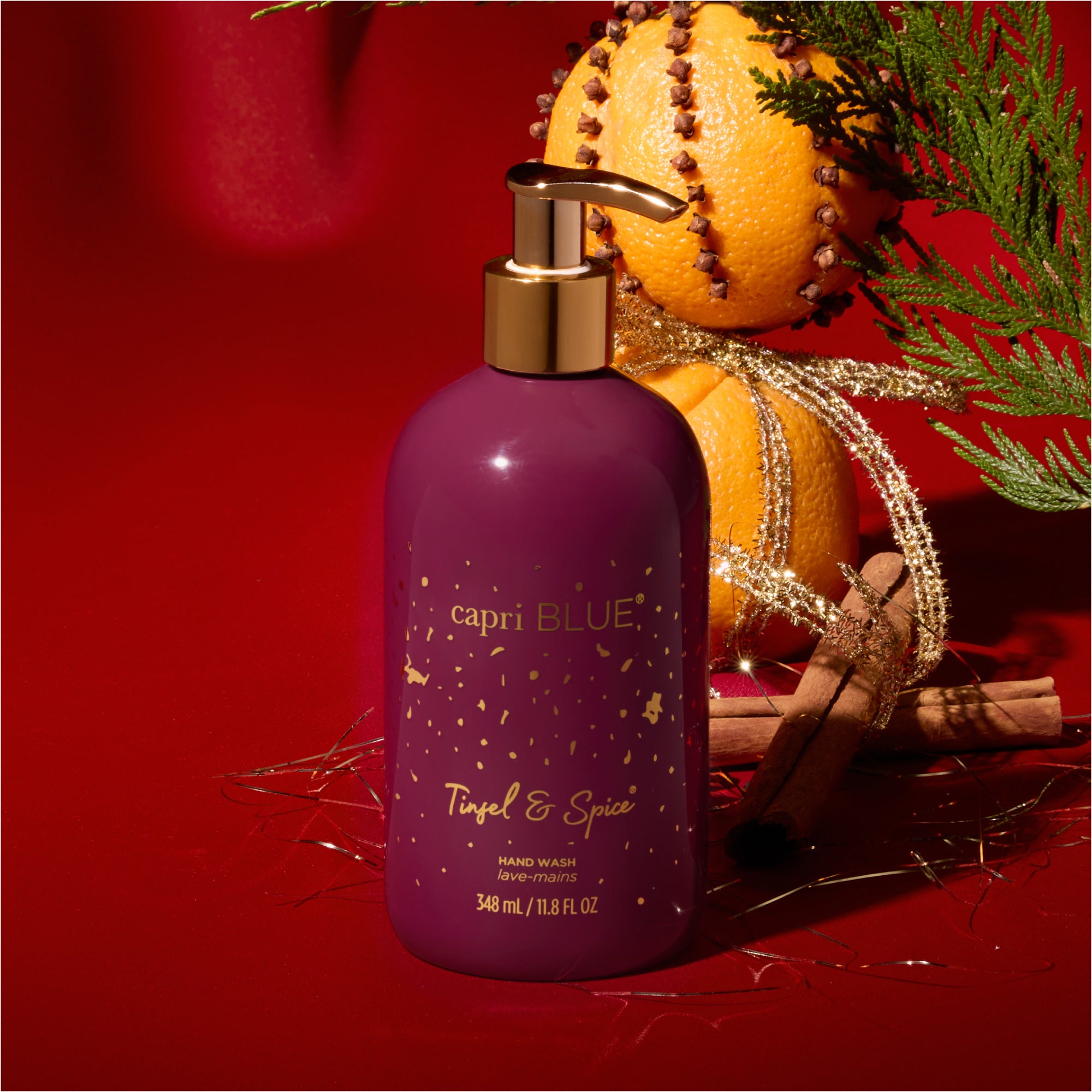 Purple bottle of capri BLUE Tinsel & Spice hand wash on a red background with pump and decorative elements.