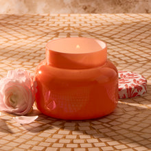 Orange ceramic jar with a candle on a mosaic tile surface
