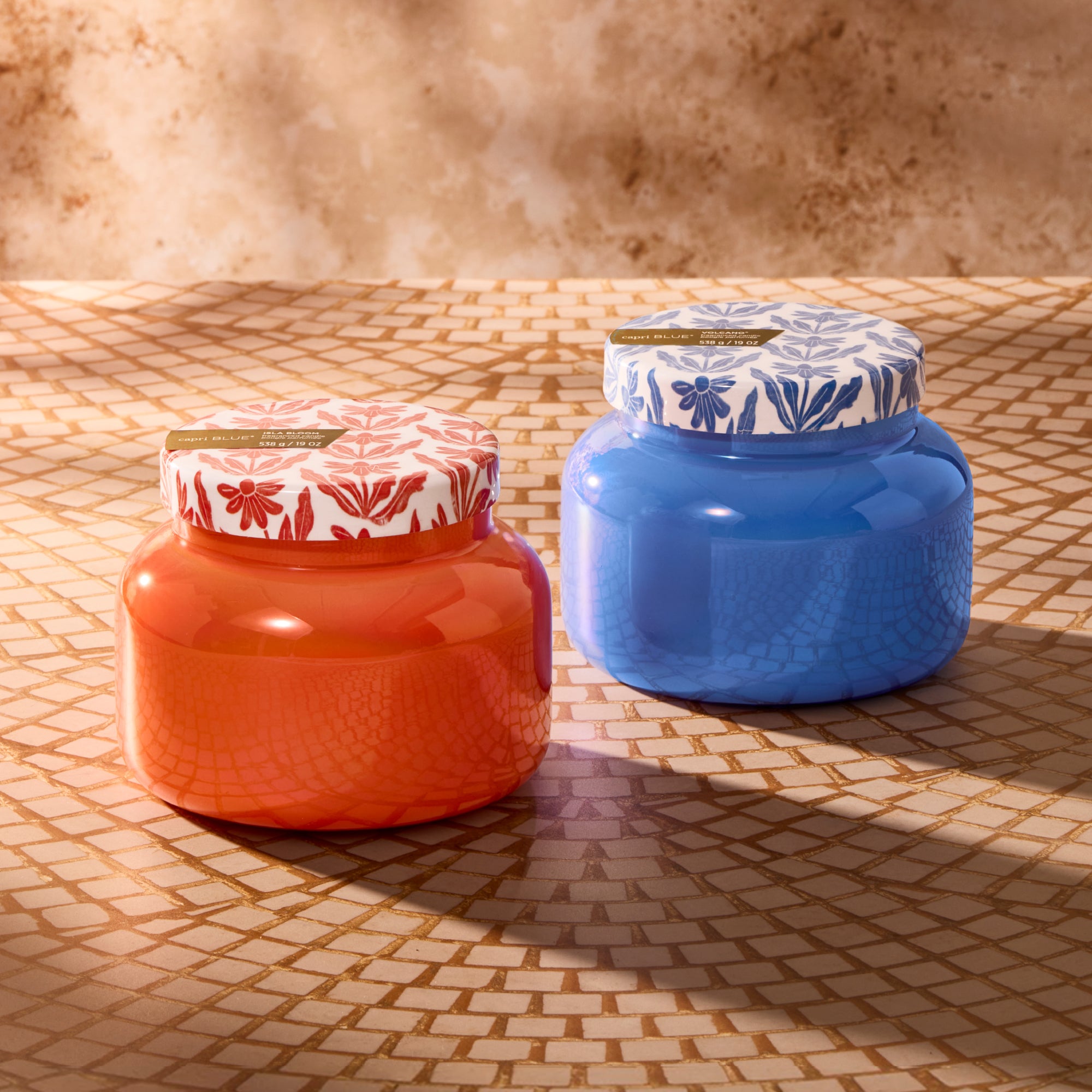 Two candles, one orange and one blue, with decorative lids on a textured surface.