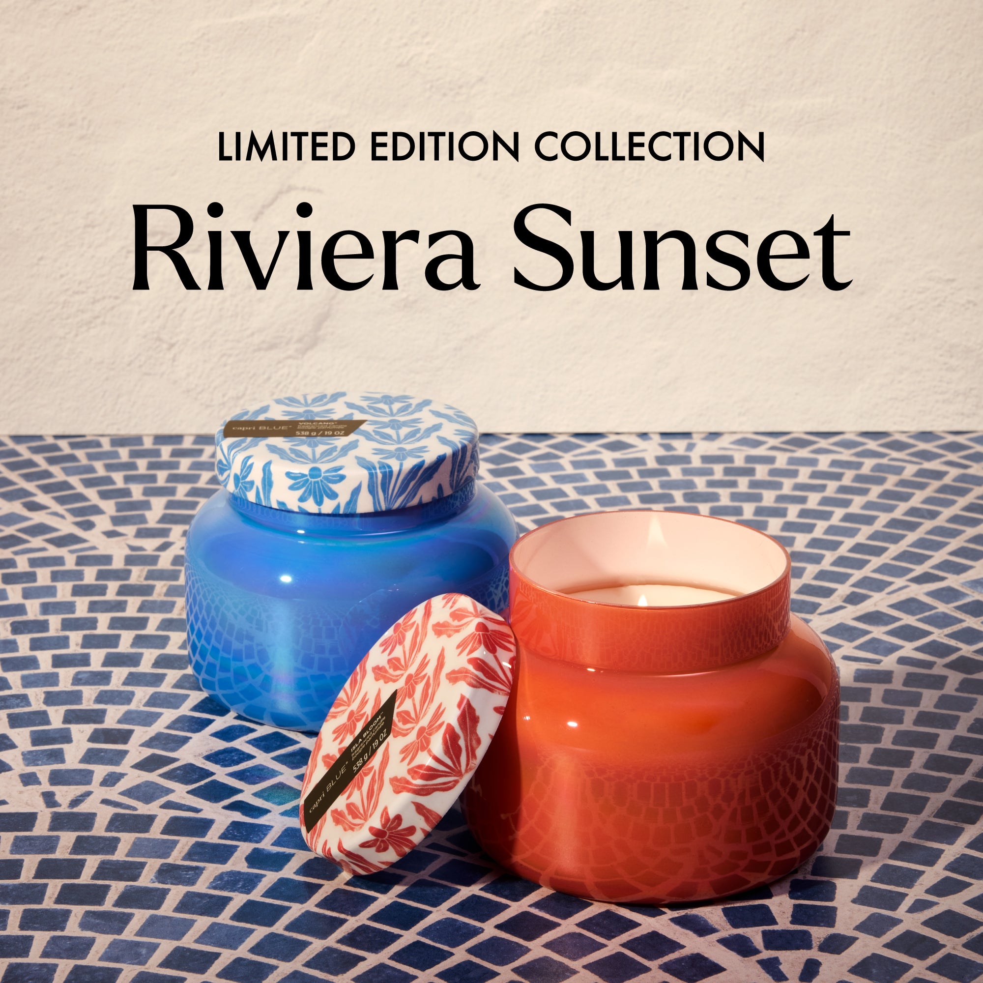 Two candles, one blue and one red, on a textured surface with 'Limited Edition Collection Riviera Sunset' text.