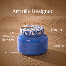 Blue glass jar with floral metal lid on a textured surface, labeled with features.