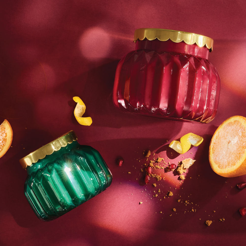 Two Royal Gem candles with gold lids on a red background with oranges and spices.