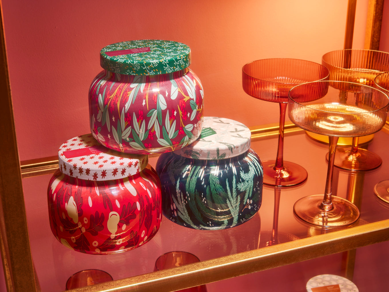 Three Holiday Pattern Play Signature candles stacked on a shelf next to champagne glasses