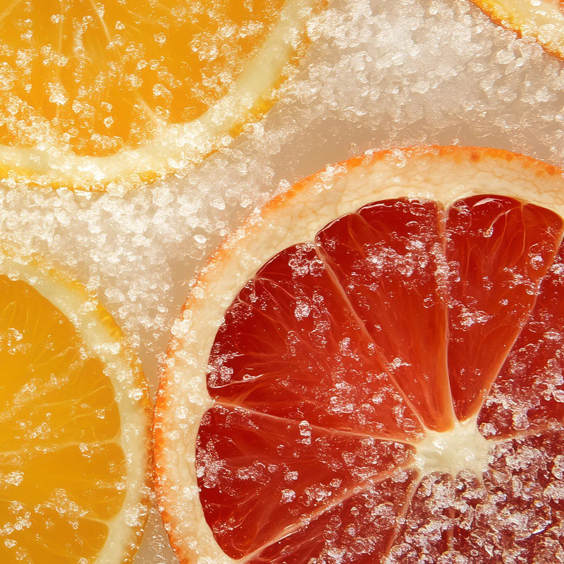 Close-up of citrus slices, including orange and red grapefruit, coated with coarse sugar crystals on a light background.