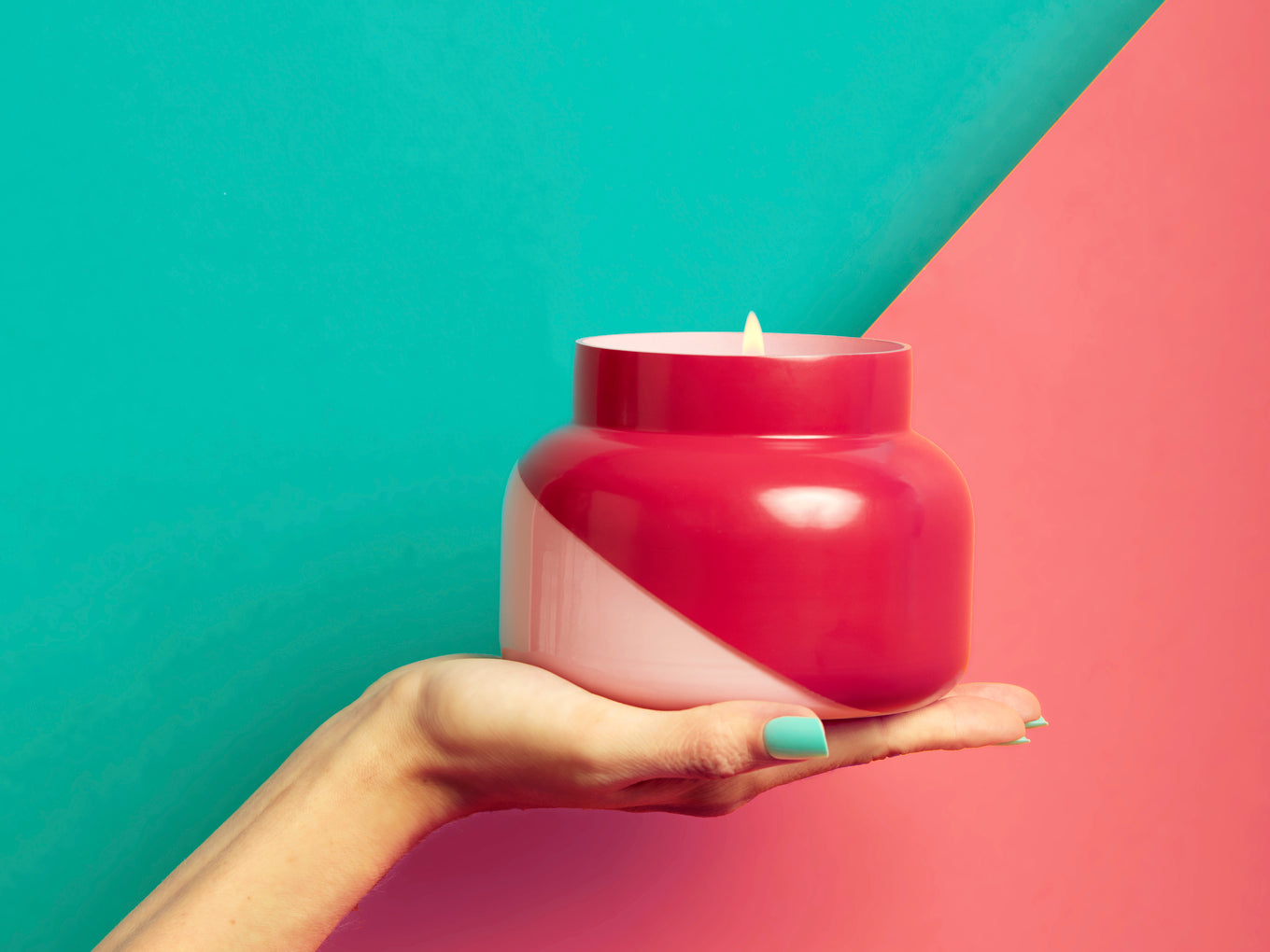 Hand holding a pink candle jar against a colorful background