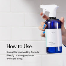 Hand holding a blue spray bottle with a white label against a tiled wall background.