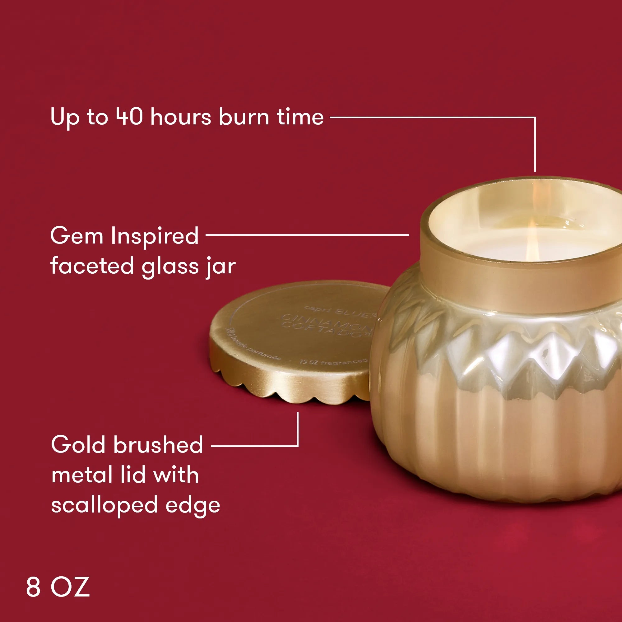 A lit, Cinnamon Cortado Royal Gem Petite Candle in a champagne-topaz  faceted glass jar wit text describing its features:  "Up to 40 hours burn time", "Gem inspired faceted glass jar", "Gold brushed metai lid with scalloped edge" and "8 oz."