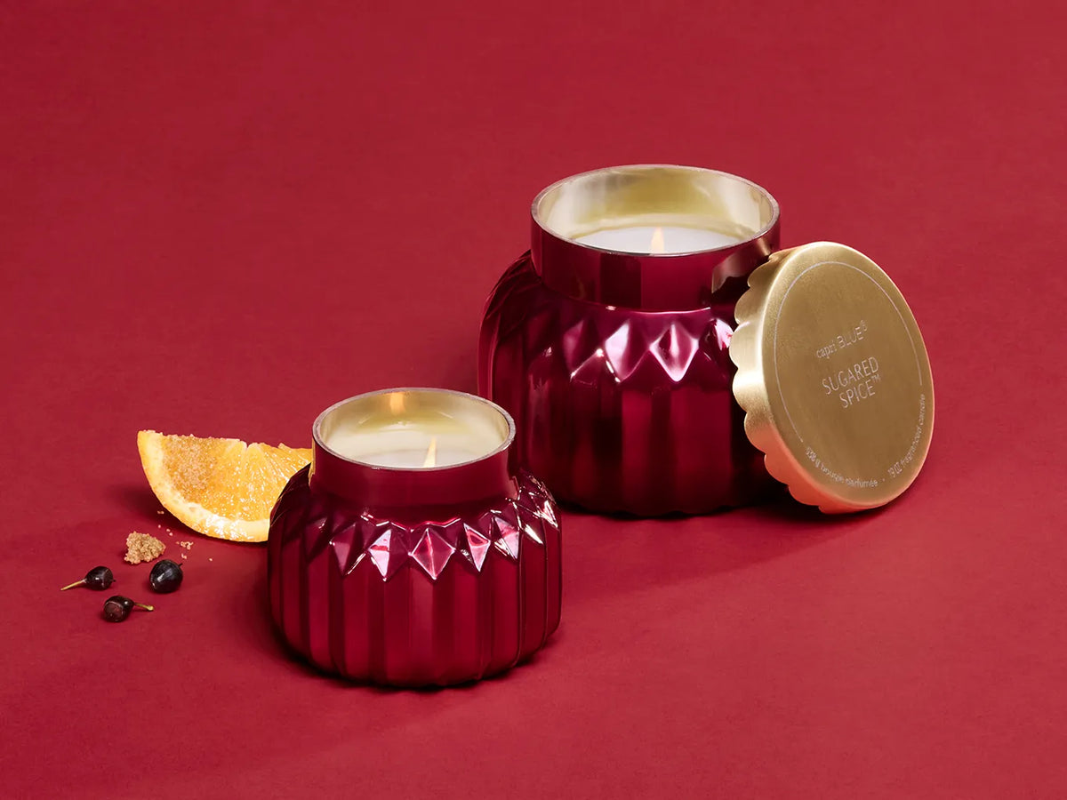 A lit, Sugared Spice Royal Gem Petite Candle beside a lit, Sugared Spice Signature Candle, orange wedges, fresh black currant, and brown sugar.