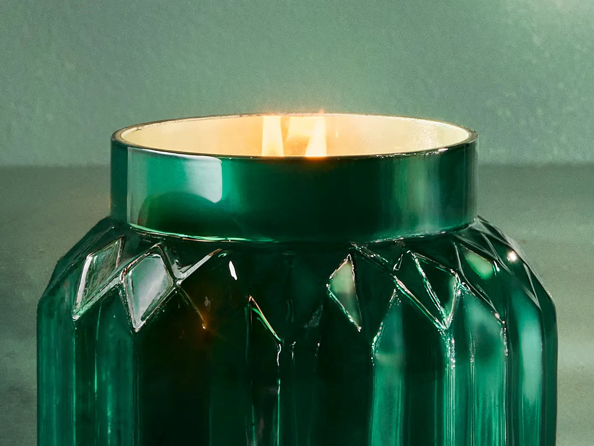 A lit, Volcano Royal Gem Signature Candle with an emerald green, gem-inspired jar.