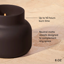 A matte black 8 oz candle holder with a lit candle, shown on a beige stone surface with text overlays highlighting its 40-hour burn time and neutral matte finish.