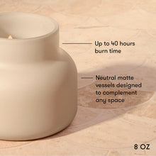 A matte ceramic candle holder or vessel in a warm off-white/cream tone, shown on a beige stone-like surface with text callouts noting up to 40 hours burn time and neutral matte vessels designed to complement any space. '8 OZ' appears in the lower right.