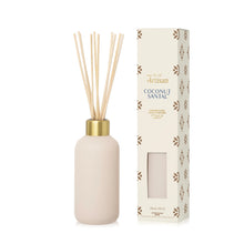A reed diffuser bottle with natural reed sticks and a gold collar, shown next to its cream-colored packaging box with brown floral patterns. The brand 'Artisan' is visible on the box.