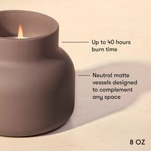 A matte taupe candle holder with a lit candle, shown on a warm beige background with text overlays highlighting its 40-hour burn time and neutral matte finish.