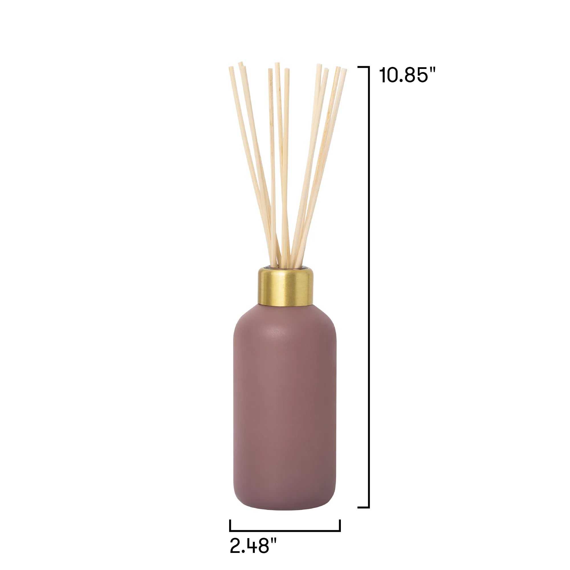 A reed diffuser bottle in a muted mauve-pink color with a gold collar and natural beige reeds, shown on a white background with black dimension lines indicating height of 10.85 inches and width of 2.
